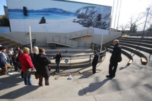 Visitors in outdoor amphitheater with seaside mural